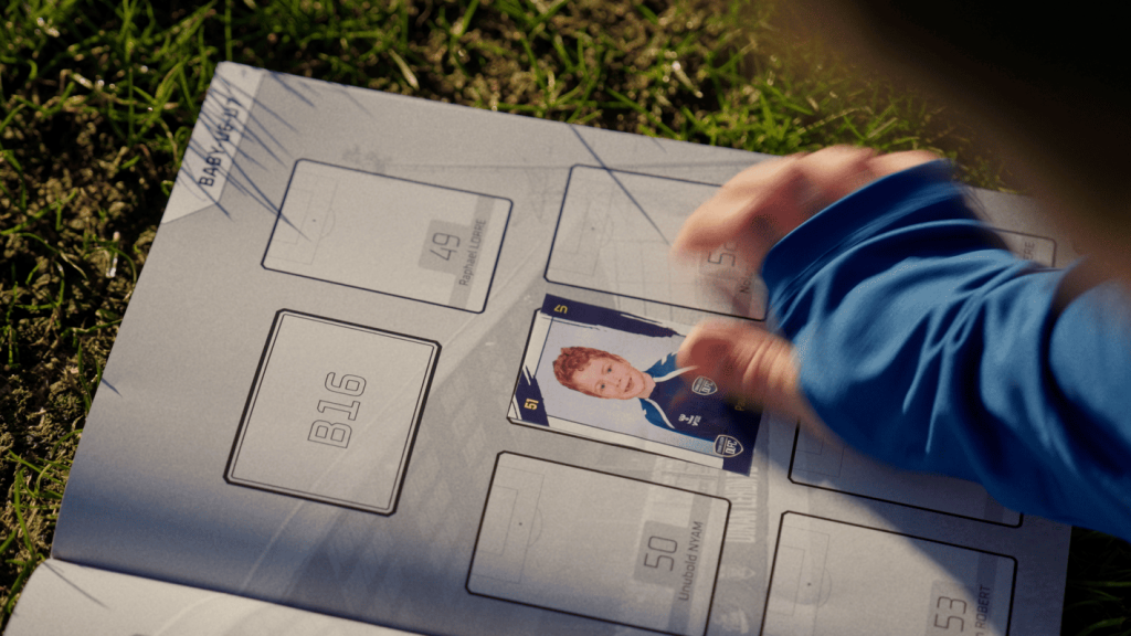 Une jeune joueuse du club du Dinan Léhon FC colle l'étiquette de l'Album du Club sur l'album du Dinan Léhon FC